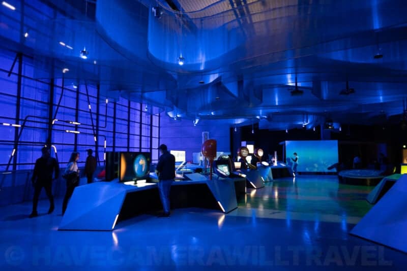 Visitors exploring glowing interactive exhibits inside a blue-lit science museum hall