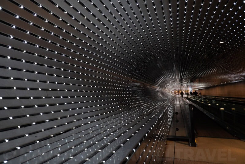 Perforated metal walkway ceiling with rows of pinhole lights creating a tunnel vanishing point