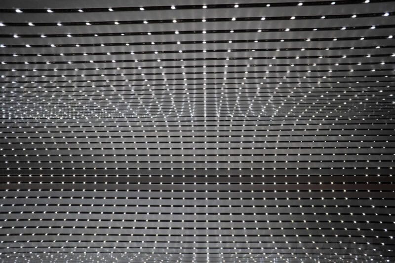 Ceiling installation of horizontal slats with rows of small pinpoint lights creating a rippling pattern