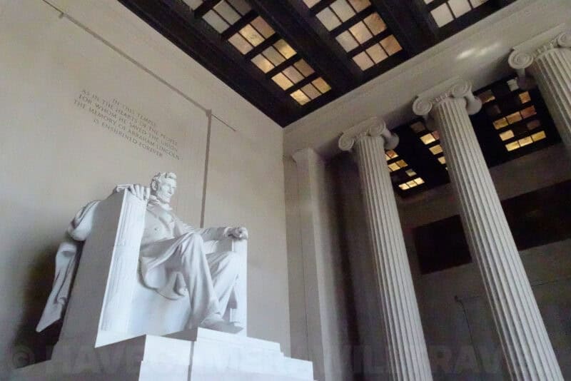 Lincoln Memorial statue seen from below beside coffered ceiling and Ionic columns