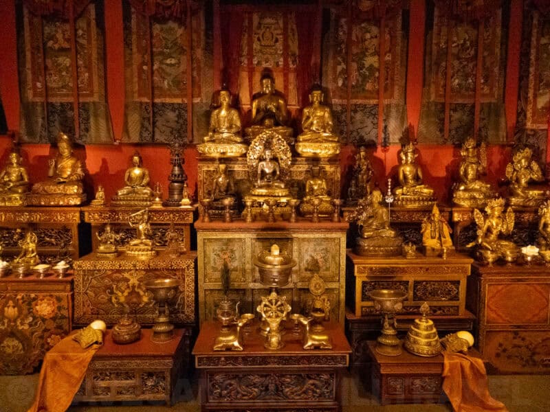Rows of gilded Buddhist statues and thangka scrolls on an ornate temple altar