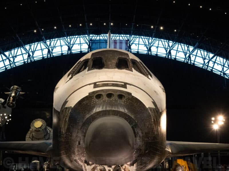 Space Shuttle's nose and cockpit windows lit beneath a curved museum roof