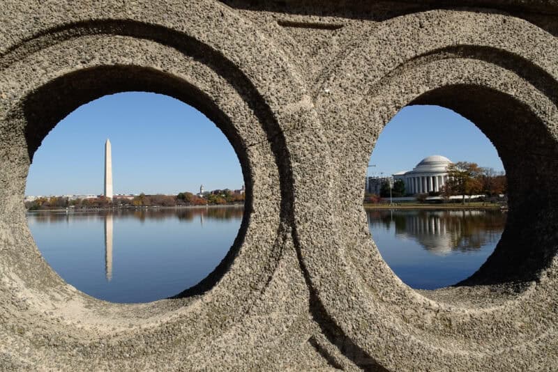 Washington Monument and Jefferson Memorial framed through circular stone openings in a balustrade