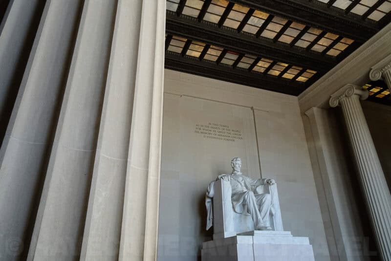 Lincoln Memorial statue viewed between marble columns beneath its stained-glass skylight ceiling