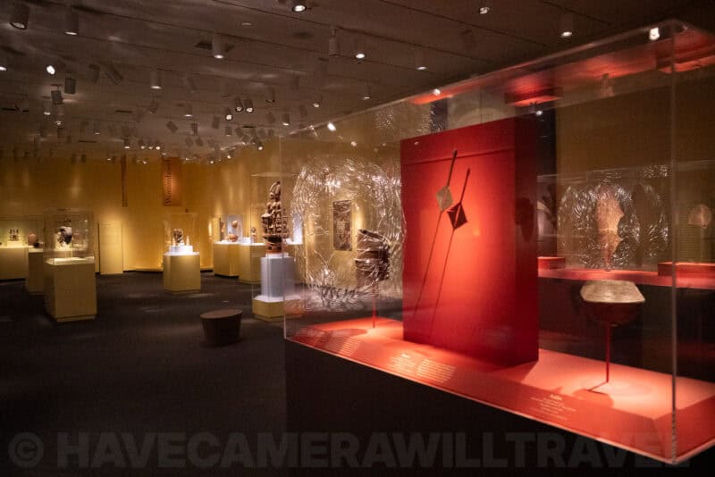 Museum gallery with illuminated red display case and artifacts in dim ambient light