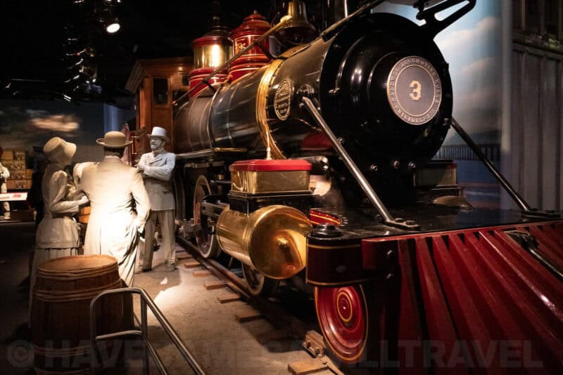 Vintage steam locomotive with polished brass fittings displayed beside costumed figures