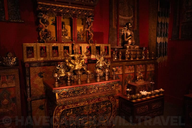 Gilded Buddhist shrine with statues and offering bowls glowing in a dim red room