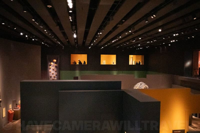 Dim museum gallery interior with illuminated display alcoves and visitors on an upper level
