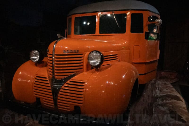 Vintage orange truck with rounded fenders parked in a dark museum display hall