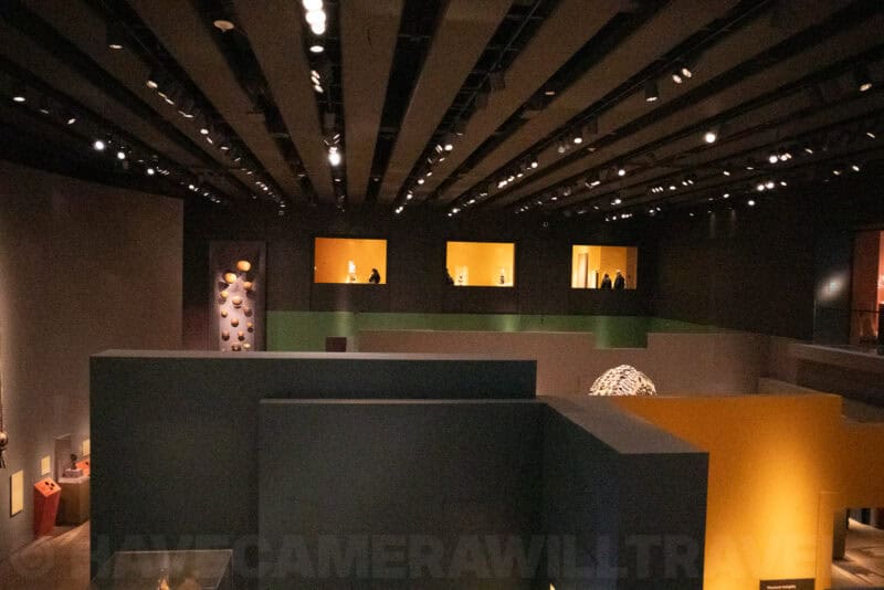 Dim museum gallery with glowing display alcoves and visitors viewed from above