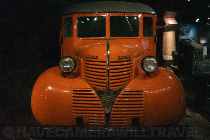 Vintage orange truck cab with round fenders on display in a dark museum hall