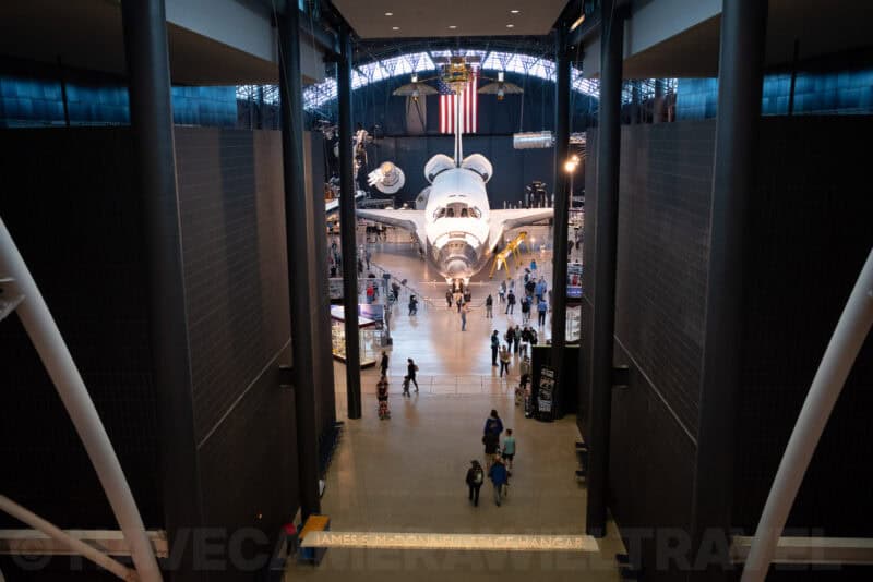 Space shuttle displayed beneath a large American flag inside a museum hangar