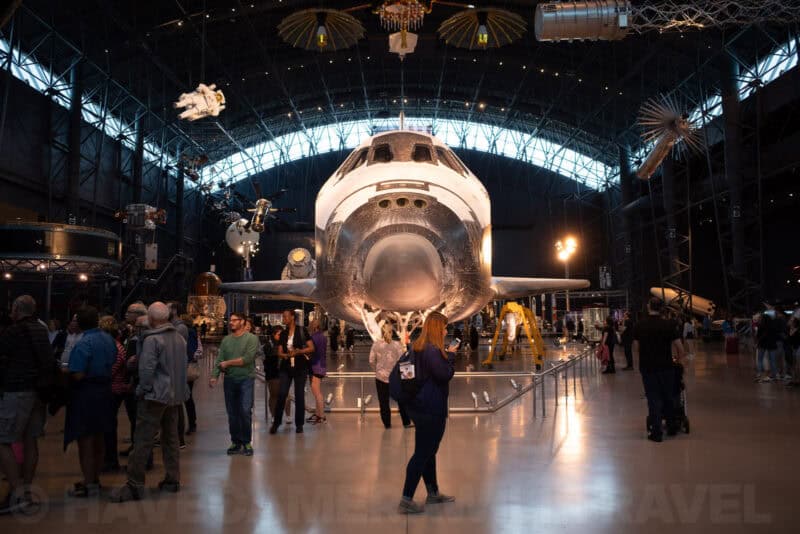 Space shuttle on display inside a museum hangar with visitors walking below