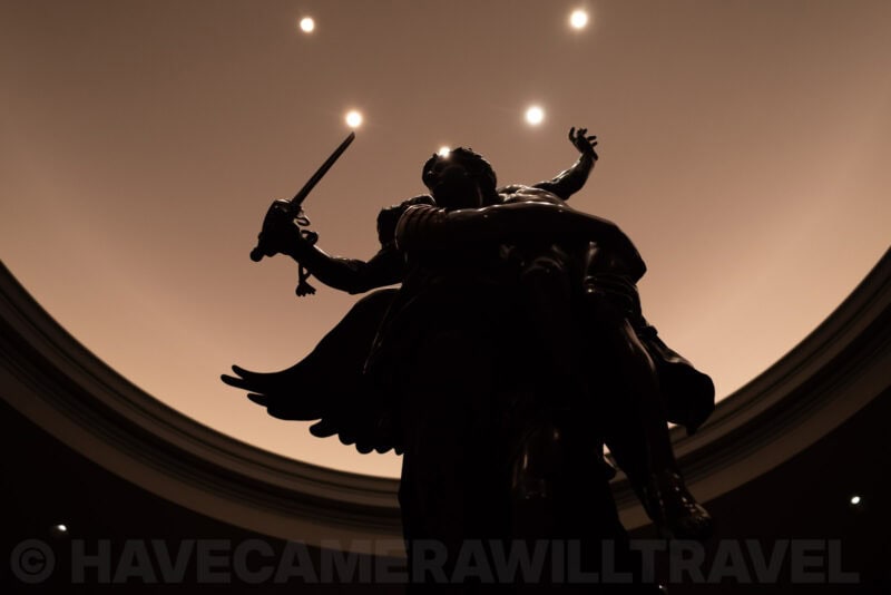 Silhouetted winged statue photographed from below against a domed ceiling