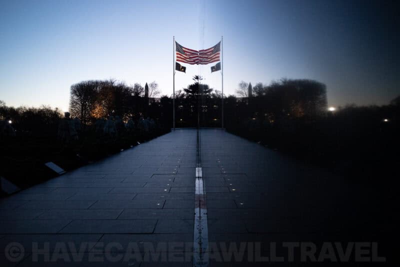 Korean War Veterans Memorial pathway with flags reflected on polished stone at dusk