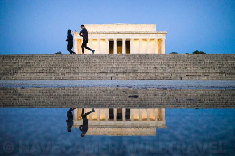 Lincoln Memorial at dusk reflected in a rain puddle on the steps as joggers pass