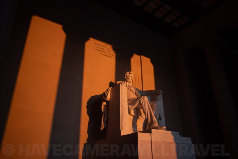 Lincoln Memorial statue lit by warm sunset light with long column shadows on the wall