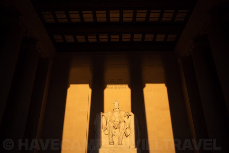 Lincoln statue glowing gold at sunrise with dramatic column shadows