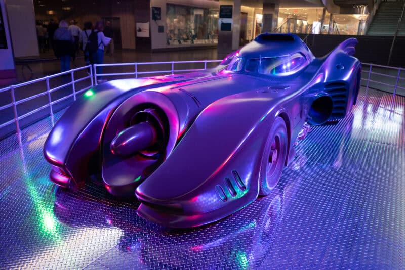 The Batmobile prop car on display under colored lights in a museum atrium