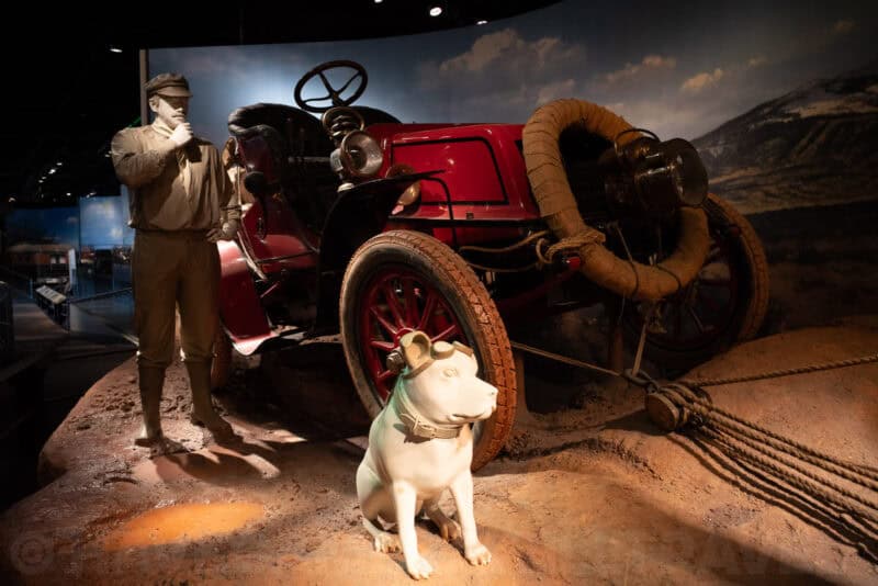 Vintage red car and a dog statue displayed in a museum diorama