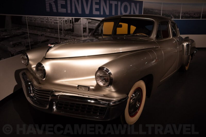 Vintage silver Tucker automobile displayed under a museum spotlight