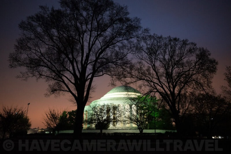 Jefferson Memorial dome glowing at dusk framed by bare winter trees