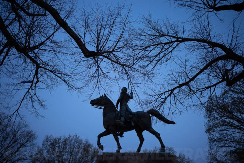 Equestrian statue silhouetted against a blue dusk sky beneath bare tree branches