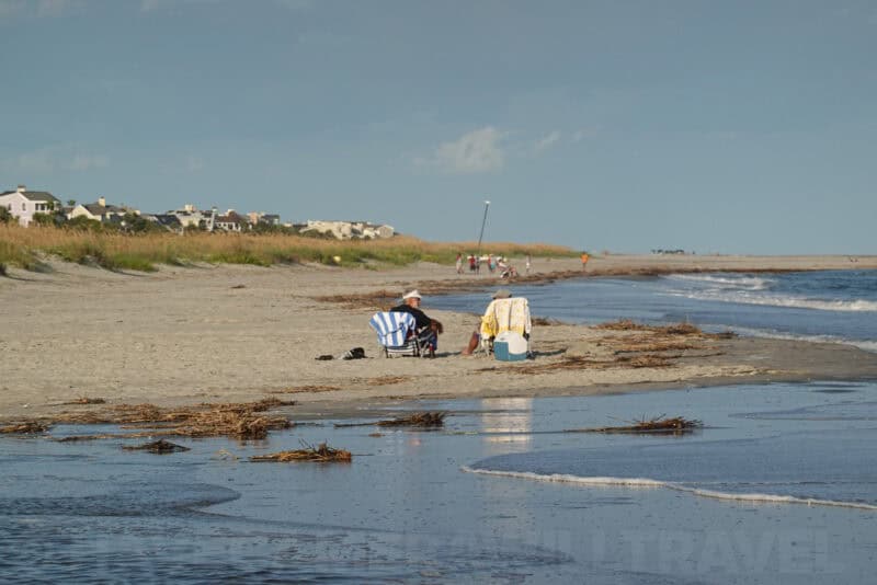 Two beachgoers in folding chairs by the shore captured at 200mm optical zoom