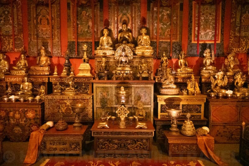 Tibetan Buddhist altar filled with golden statues, ritual bowls, and hanging fabric banners