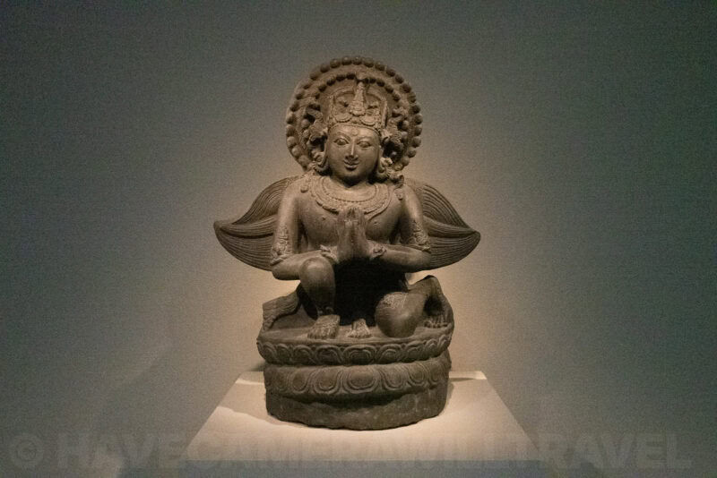 Carved stone statue of a seated deity with an ornate halo and folded-hands gesture