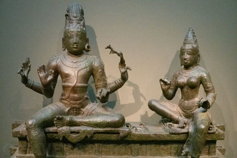Bronze statues of a seated Hindu god and goddess couple displayed in a museum gallery