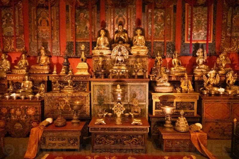 Gilded Buddhist shrine with tiered statues, offering vessels, and patterned scroll paintings