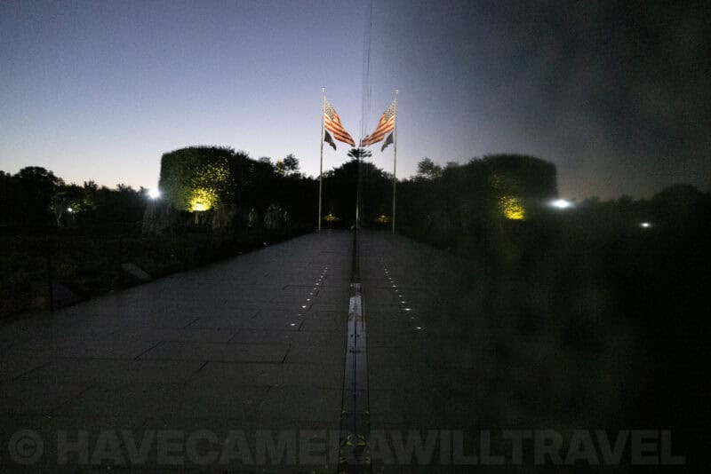 Korean War Veterans Memorial pathway with American flags reflected on a polished black wall at dusk