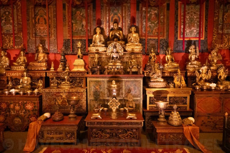 Rows of gilded Buddhist statues and ceremonial objects arranged on an ornate temple altar