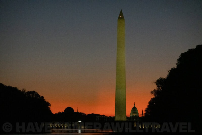 Washington Monument towering above the Capitol dome against a glowing orange dusk sky