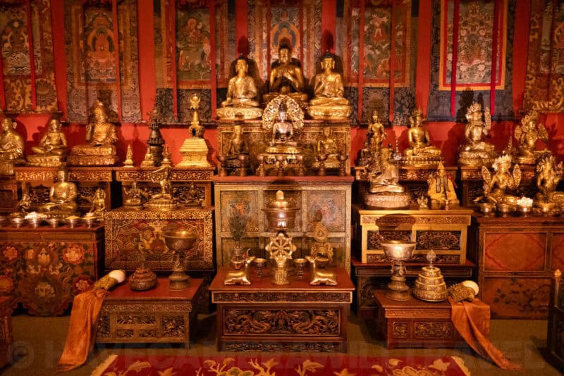 Golden Buddhist shrine display with tiered statues, ritual vessels, and colorful hanging scrolls