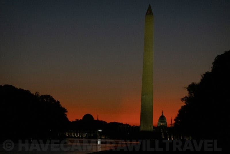 Washington Monument silhouetted against an orange sunrise sky with the US Capitol dome in the distance