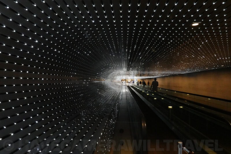 Illuminated tunnel escalator lined with sparkling star-like ceiling lights