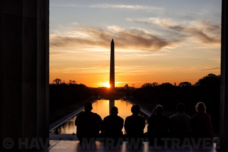 Silhouetted onlookers watching the sun set behind the Washington Monument over the reflecting pool