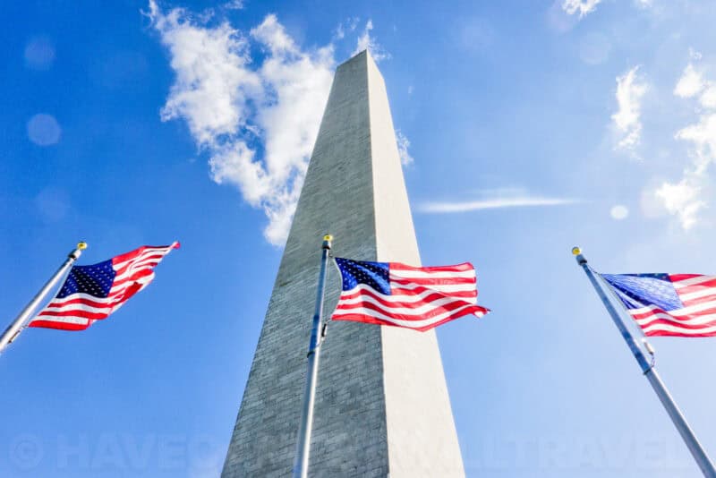 Washington Monument towering against a blue sky with American flags waving below