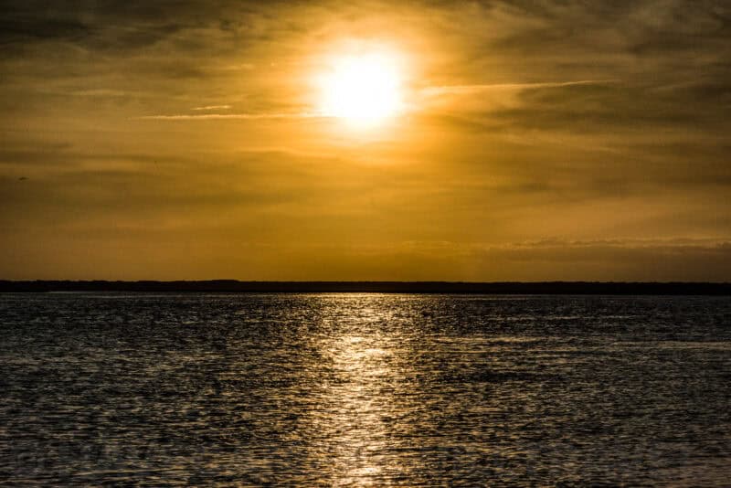 Sun reflecting on rippling water beneath a hazy golden sky at dusk