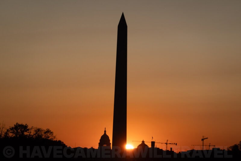 Washington Monument silhouetted against an orange sunrise with the Capitol dome nearby