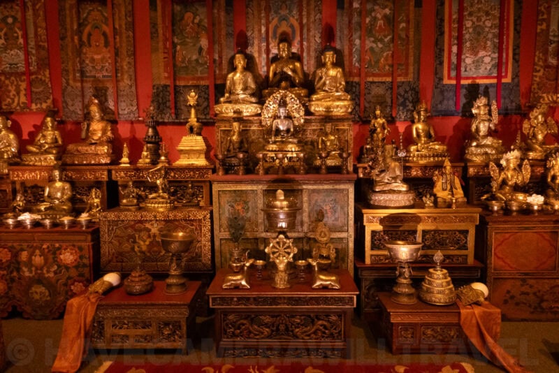 Gilded Buddhist statues and ritual objects displayed on an altar in dim lighting