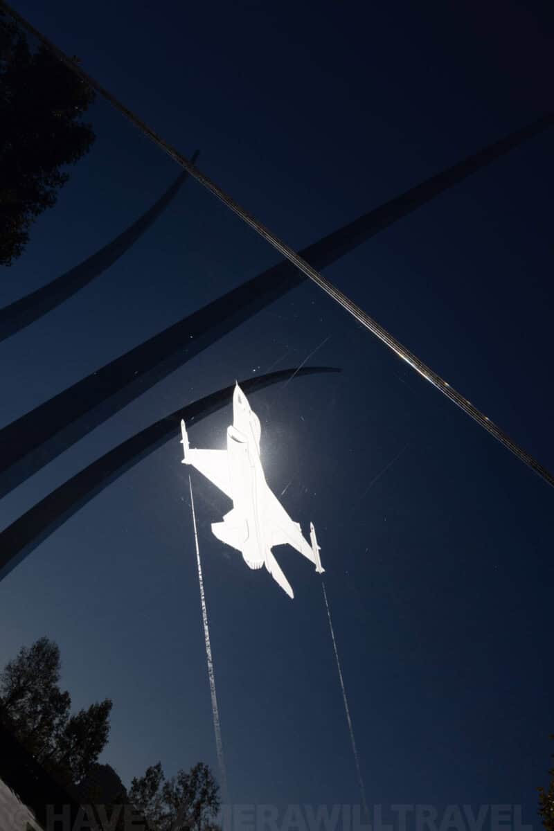 Air Force Memorial's steel spires framing a fighter jet reflection against a dark blue sky