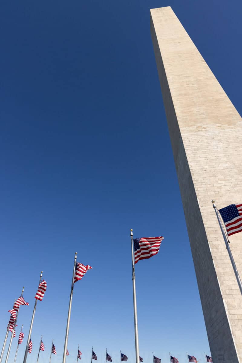 Washington Monument obelisk viewed from below with rows of American flags fluttering