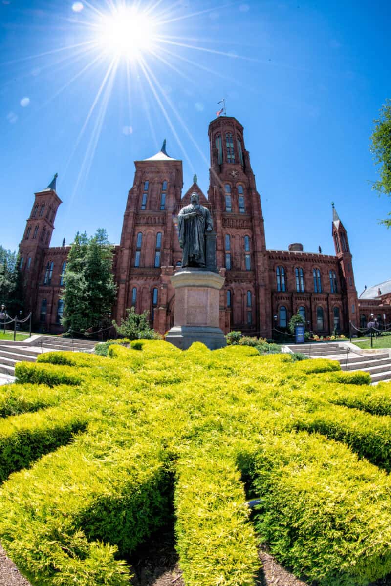 Sunburst over the red sandstone towers of the Smithsonian Castle behind a statue and hedge maze