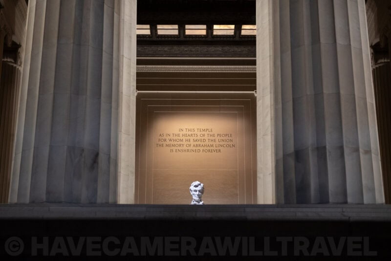 Lincoln Memorial statue framed between marble columns, inscription visible on the wall behind