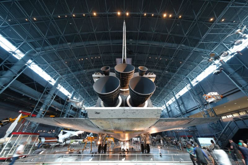 Space shuttle's tail and engine nozzles viewed from below inside a large museum hangar