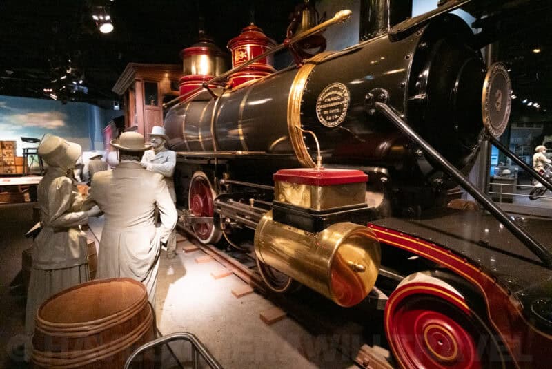Vintage steam train with brass fittings and red wheels beside costumed mannequins, ISO 25600 image