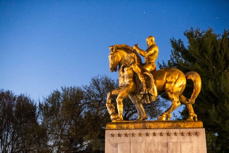 Golden equestrian statue of a rider on horseback glowing under floodlights against a dusk sky with visible stars